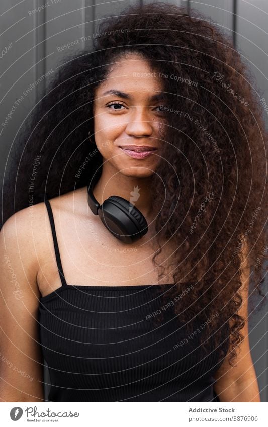 Charmante ethnische Frau mit Kopfhörer auf der Straße krause Haare Afro-Look Frisur charmant Lächeln natürlich Schönheit schwarz Afroamerikaner Großstadt trendy