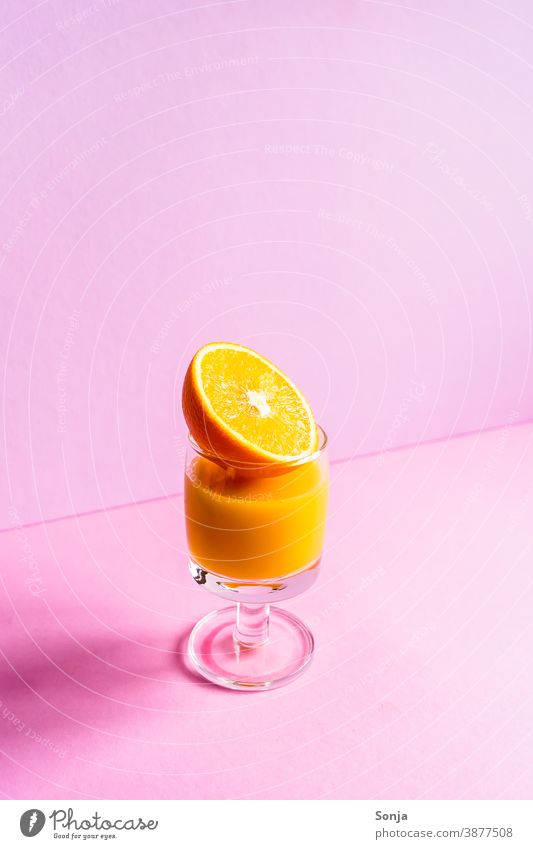 Ein Glas Orangensaft mit einer halbierten Orange auf einem isolierten rosa Hintergrund orange Getränk Zitrusfrüchte Saft frisch Obst Erfrischung Früstück