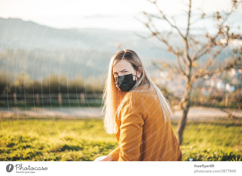 Frau im gelben Mantel auf einer Bank sitzend mit Gesichtsmaske Sitzen Coronavirus COVID Winter Herbst betrachtend Vigo Galicia Natur im Freien Freiheit