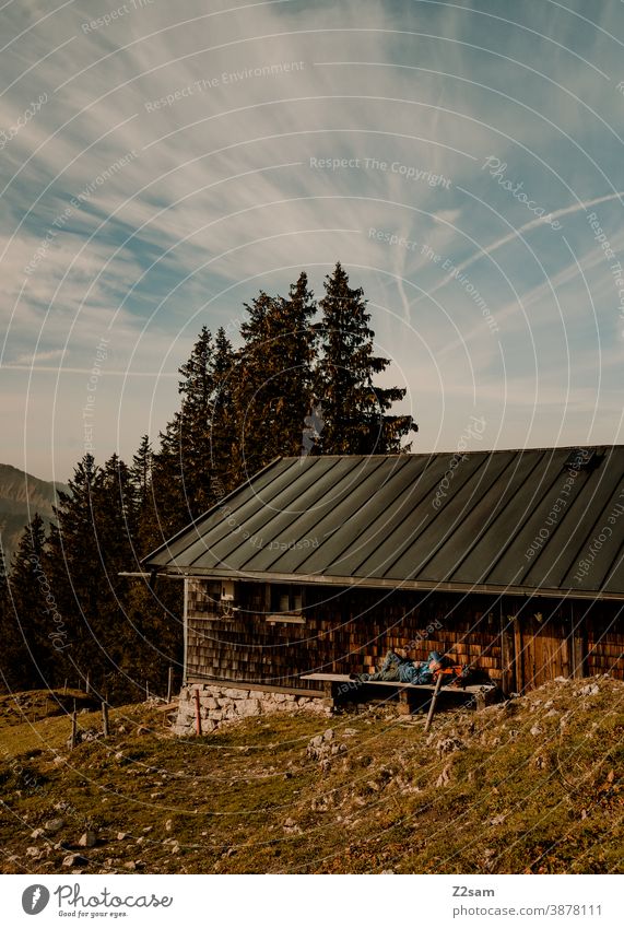 Wanderer liegt zum Sonnen auf einer Bank einer Berghütte spitzing wandern herbstfarben outtdoor ausflug wandertour Berge u. Gebirge alpen bayern himmel blau