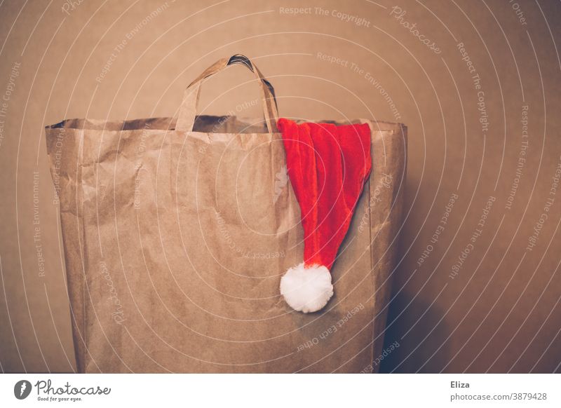 Papiertüte aus der eine Nikolausmütze herausguckt. Weihnachtshopping. Weihnachten Weihnachtsshopping einkaufen Tüte Einkaufstüte Weihnachtsmann
