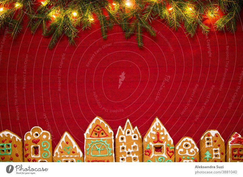 Hintergrund zu Weihnachten. Rote Tischdecke mit einer Stadt mit niedlichen Lebkuchenhäusern, die mit Zuckerguss, Weihnachtsbeleuchtung und Glitter dekoriert sind. Feiertagsstimmung.