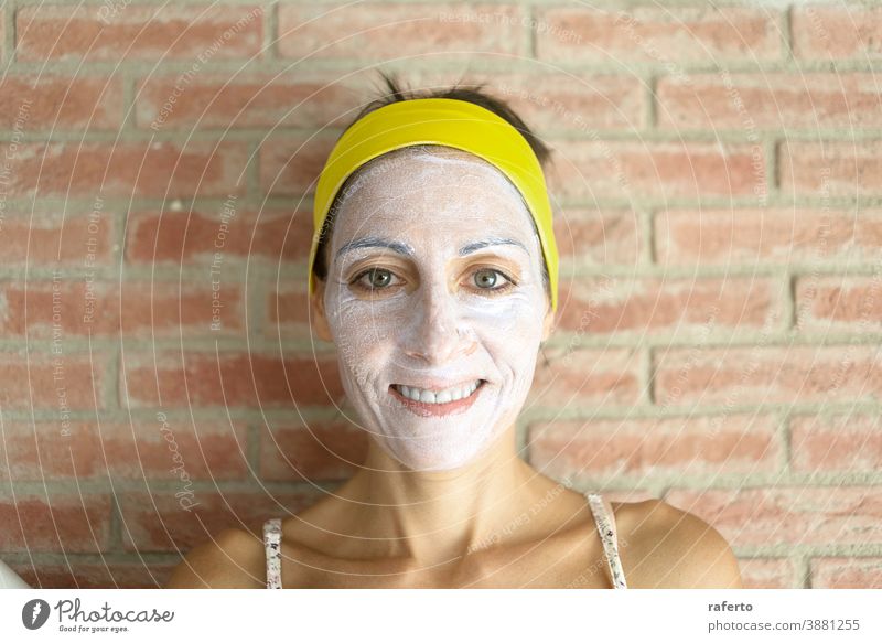 Entspannte Frau trägt zur Verjüngung eine Mineral-Ton-Maske auf das Gesicht auf und trägt ein Stirnband am Kopf Hautpflege Mundschutz Kosmetik Pflege