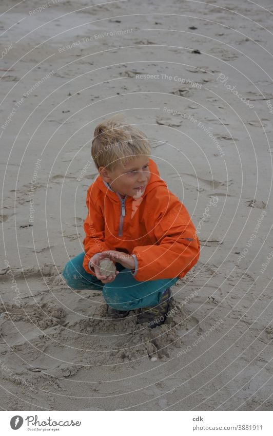 Kindheit | sandige Angelegenheit. Junge blond in der Hocke im Sand am Meer orange Windjacke türkis Ferien Sandkugel formend beobachtend Ferien & Urlaub & Reisen
