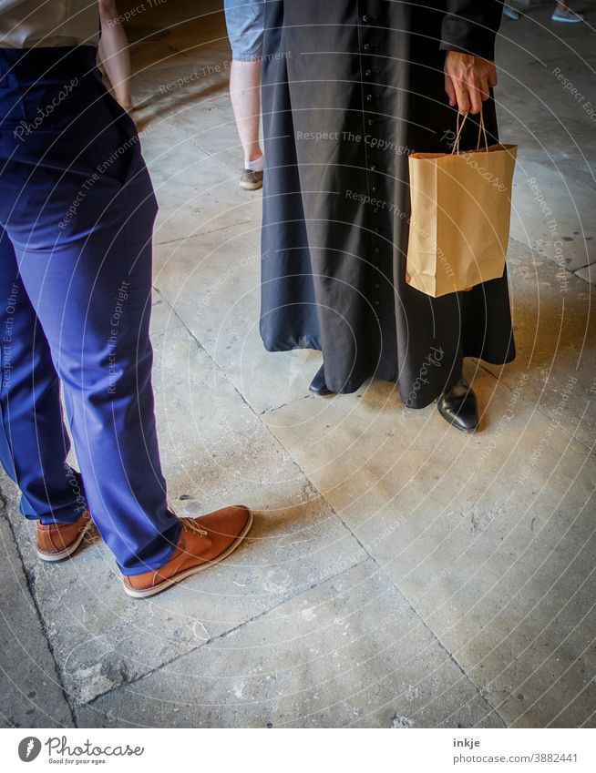 Mann in Talar mit Papiertasche und Mann in Stoffhose stehen sich gegenüber Farbfoto Menschen Hose Schuhe Gespräch Kommunikation Geistlicher Unterhaltung