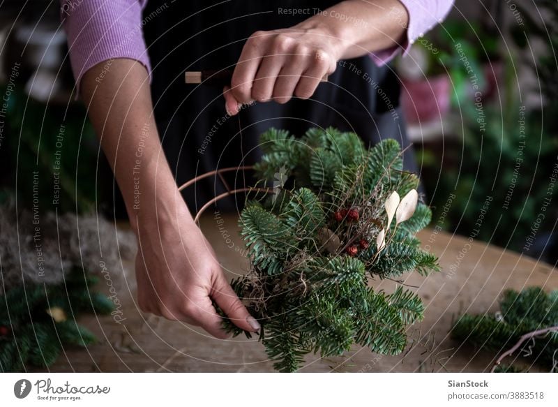 Frau macht Weihnachtskranz aus Fichtenholz, Schritt für Schritt. Konzept der Arbeit des Floristen vor den Weihnachtsfeiertagen. Hand Herstellung Hände Holztisch