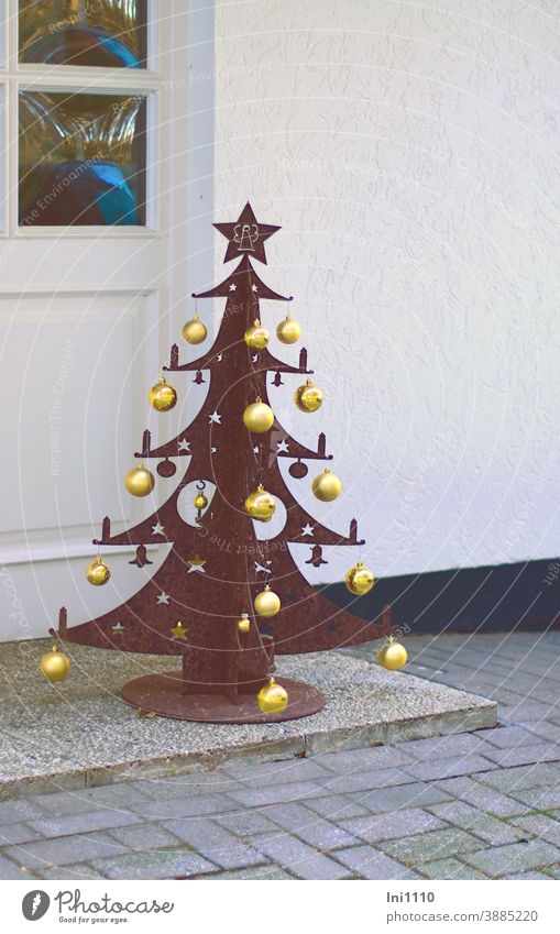 mit goldenen Kugeln behängter Weihnachtsbaum aus rostigem Metall steht vor weißem Hauseingang Weihnachtsdekoration Meltall rostiges Metall goldene Kugeln