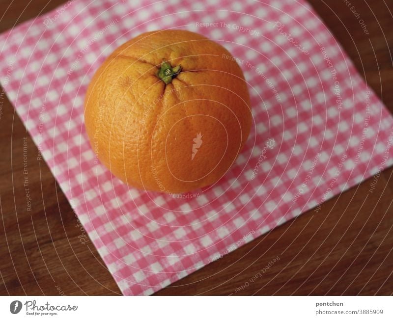 Eine orange liegt auf einer karierten Serviette auf einem Tisch. Vitamin C, gut fürs Immunsystem Orange Zitrusfrucht Gesundheit Frucht Vitamin c frisch Obst