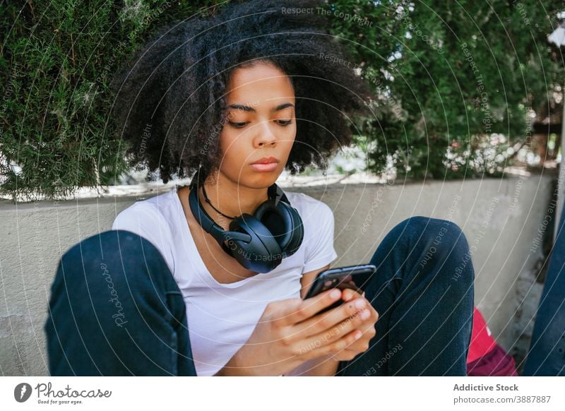 Junge ethnische Frau nimmt Selfie in der Stadt Kopfhörer Straße Selbstportrait urban Afro-Look Frisur unterhalten emotionslos schwarz Afroamerikaner Großstadt