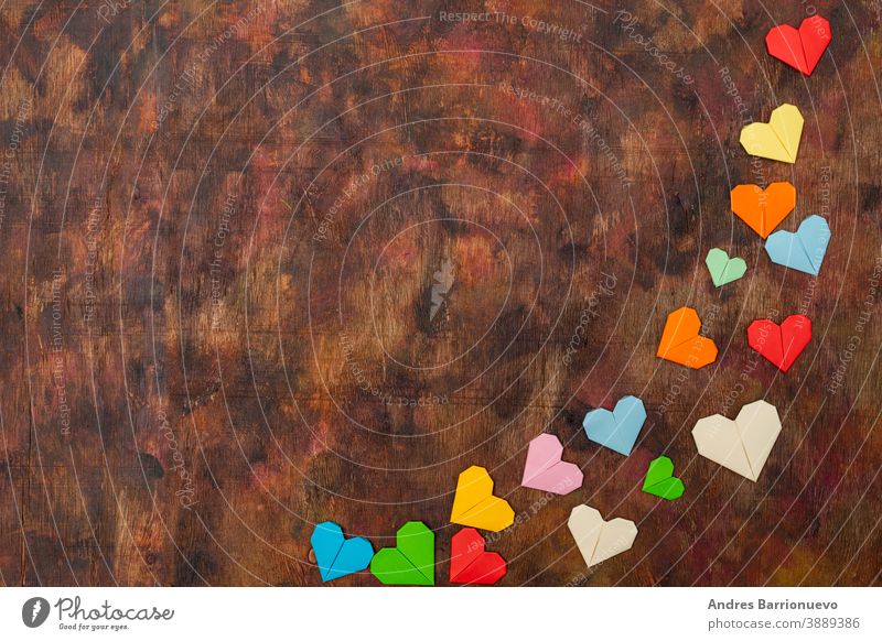 Origami-Herzen aus farbigem Papier zur Gratulation zum Valentinstag für verliebte Paare, auf altem Holzuntergrund in Brauntönen Holzplatte grün hölzern