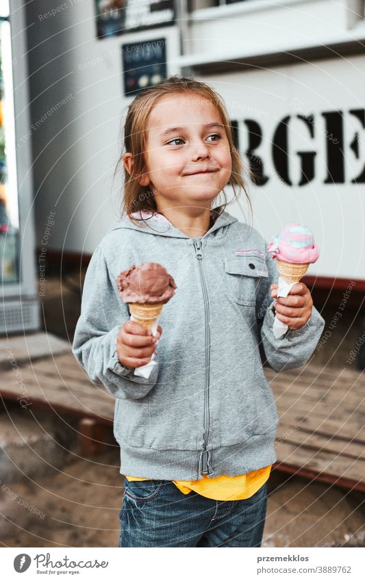 Glücklich lächelndes kleines Mädchen hält zwei Eiscreme vor einem Speisewagen Urlaub Familienzeit Familienurlaub Zeit verbringen Ausgaben kaufen Werkstatt Café