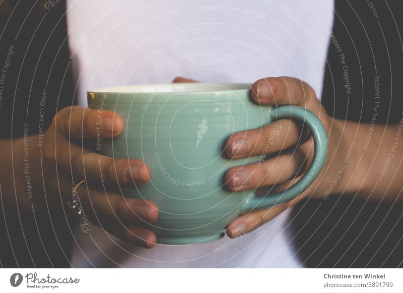 Nahaufnahme einer großen hellgrünen Tasse mit Kaffee oder Tee in den Händen einer jungen Frau. Becher halten festhalten schwarz weiß Getränk Teetasse