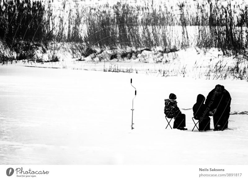auf einem zugefrorenen Fluss. Kindern beibringen, wie man im Winter Fische fängt. Eisangeln schwarz auf weiß kalt Frost Schnee Baum Lehre Lernen Vater Familie