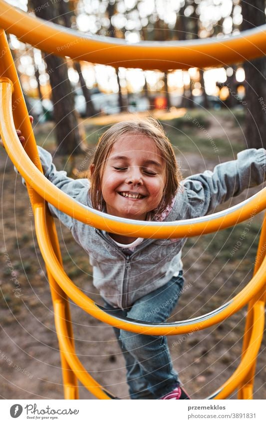 Verspieltes glückliches Mädchen im Vorschulalter, das auf einem Spielplatz auf Affenstangen klettert und mit geschlossenen Augen lächelt positiv freudig Junior