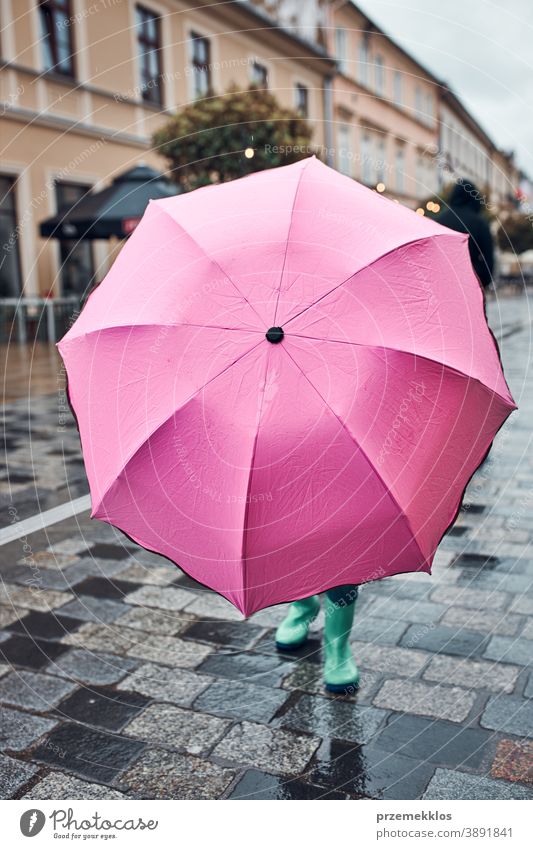 Kind, das sich hinter einem großen rosa Regenschirm versteckt und an einem regnerischen, düsteren Herbsttag in der Innenstadt spazieren geht regnet im Freien