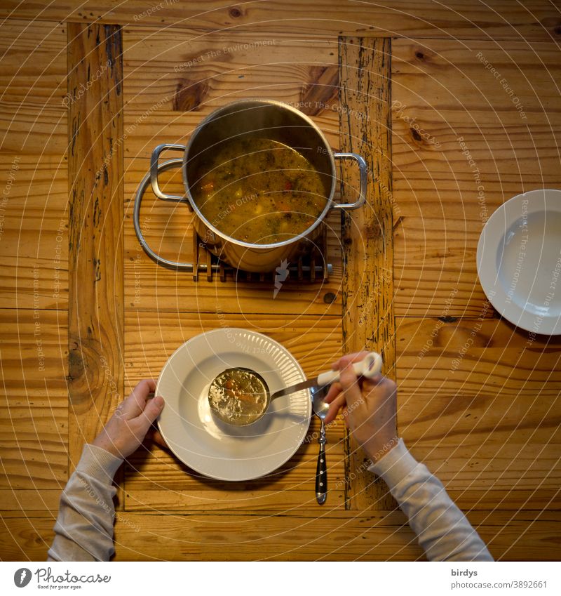Suppe austeilen, servieren. Gedeckter Holztisch mit Suppentopf, Suppenkelle, Teller und Löffeln. Vogelperspektive Eintopf essen Hände Arme Mittagessen löffeln