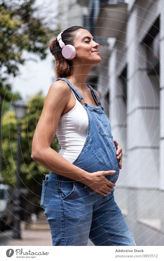 Sorglose schwangere Frau hört Musik in der Stadt zuhören Schwangerschaft Großstadt sorgenfrei berühren Bauch Kopfhörer Drahtlos Straße pränatal Gerät Dame