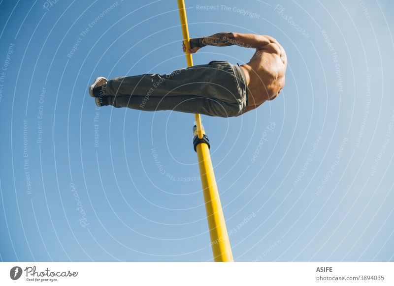 Junger athletischer Mann turnt am Barren in einem Gymnastikpark calisthenics Sport Athlet Muskeln Stärke Kunstturnen Straße Freestyle pirouettieren herumwirbeln