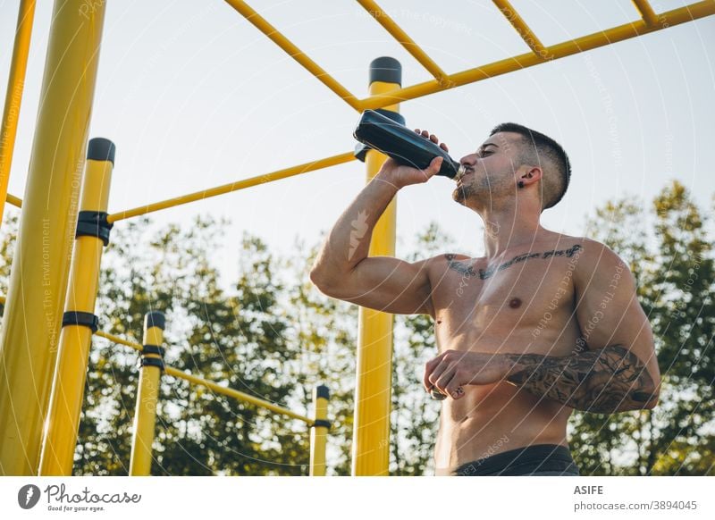 Junger Stadtsportler trinkt Wasser in einer Gymnastikhalle im Freien calisthenics Sport Athlet Mann trinken Flasche Muskeln Stärke Kunstturnen Straße Freestyle