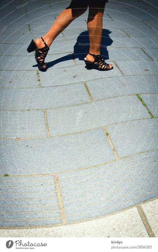 Frau mit schlanken , sonnengebräunten Beinen geht auf einem wellenförmig gepflastertem Weg Lifestyle gehen Sommer Wärme Sandalen nackte beine Bewegung