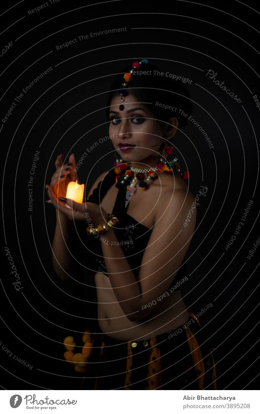 Bildnis einer indisch-bengalischen brünetten Frau in traditioneller indischer Stammes-/Dorfbewohner-Kleidung und handgemachten Ornamenten mit Kerze in dunklem Kopierraum-Atelierhintergrund. Indische Lifestyle- und Modefotografie.