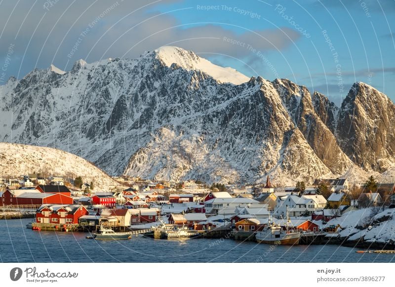 Reine auf den Lofoten im Sonnenlicht vor verschneiten Bergen Norwegen Skandinavien Fischerdorf Dorf Ort Ortschaft Kleinstadt Berge u. Gebirge Winter Schnee