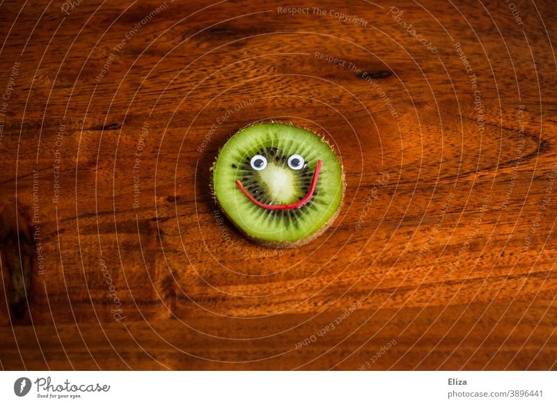 Eine Scheibe Kiwi mit lachendem Gesicht - Gesunde Ernährung gesund Vitamine Vitamin C Frucht Obst vitaminreich fruchtig lustig grün rund Holz