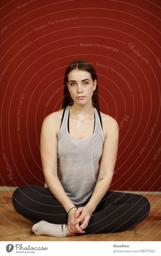 Portrait einer jungen, sportlichen Frau in Sportsachen in einem Raum vor roter Wand Studentin anmutig Schmuck Gesichtsausdruck Empathie Blick in die Kamera