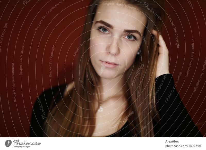 Portrait einer jungen Frau in einem Raum mit roter Wand Studentin anmutig Schmuck Gesichtsausdruck Empathie Blick in die Kamera Textfreiraum links Nahaufnahme
