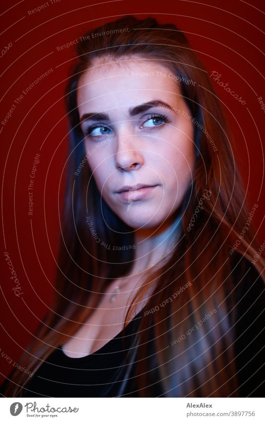 Portrait einer jungen Frau in einem Raum vor roter Wand mit rotem und blauem Licht Studentin anmutig Schmuck Gesichtsausdruck Empathie Blick in die Kamera