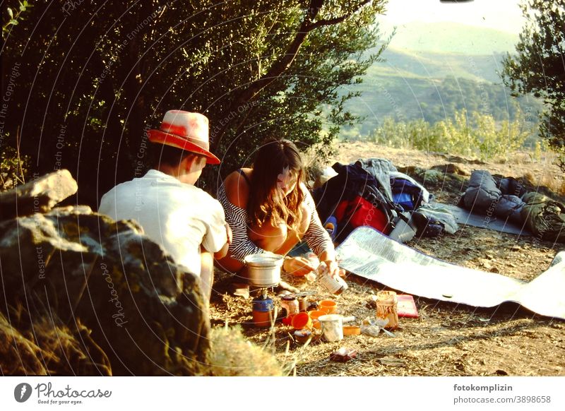 junge Frau und junger Mann beim Camping Kochen in warmer südländischer Landschaft Paar roadtrip Campingplatz Essen zubereiten Sommer Abenteuer Mann und Frau