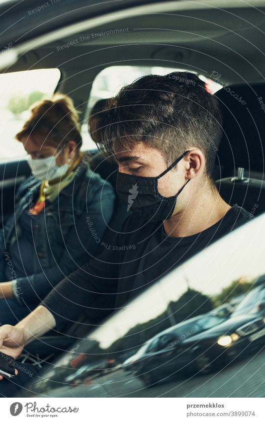 Mann und Frau sitzen in einem Auto und benutzen Smartphones und tragen die Gesichtsmasken, um eine Virusinfektion zu vermeiden Kaukasier covid-19 Lifestyle