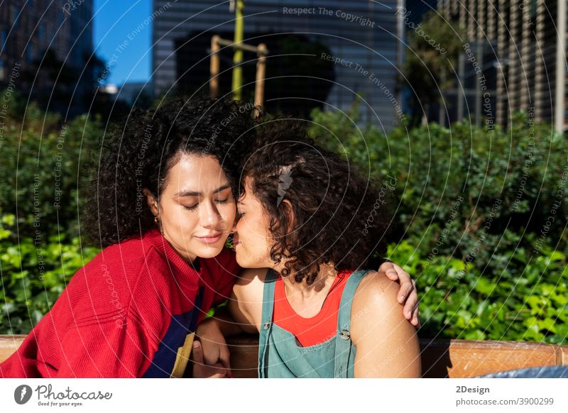 Lächelndes lesbisches Paar, das sich auf einer Parkbank umarmt und entspannt anhänglich Nähe umarmend ethnisch Ethnizität Freunde Freundschaft Lachen Liebhaber