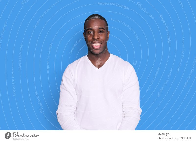 Lächelnder junger afroamerikanischer Mann in lässigem weißem Pullover, der isoliert auf pastellblauem Hintergrund auf einem Studioporträt posiert. Menschen aufrichtige Emotionen Lifestyle-Konzept. Mock up Kopierraum. Blick in die Kamera.