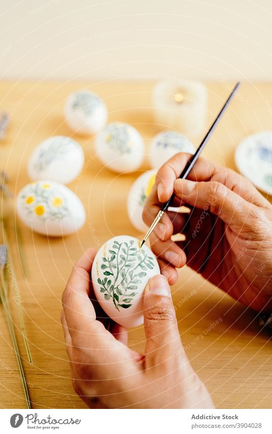 Crop Artist bemalt Eier für Ostern Anstreicher Farbe religiös Feiertag vorbereiten Kunstwerk Blume Frühling Aquarell Lebensmittel Tradition Tisch Religion Dekor