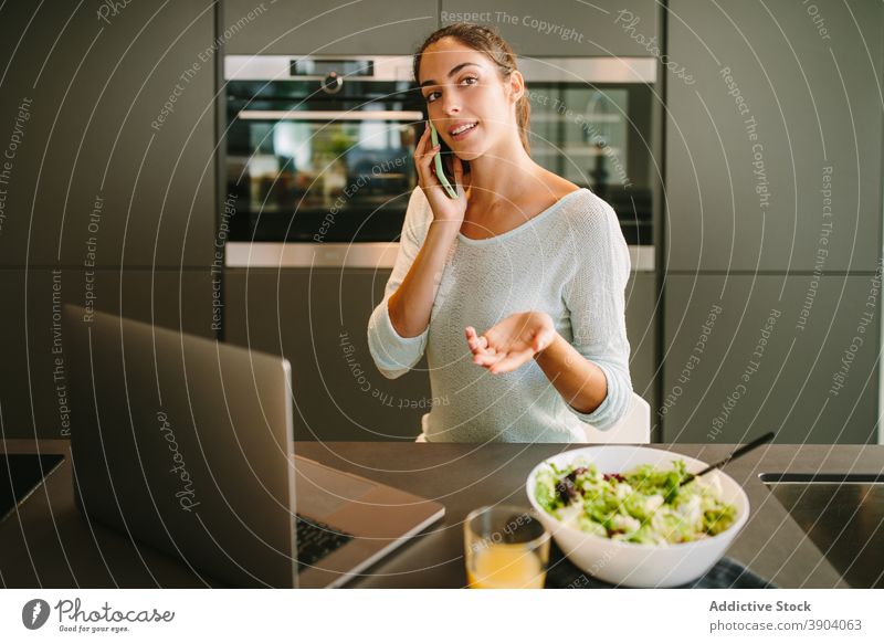 Frau spricht auf Smartphone in der Küche sprechend zu Hause Laptop abgelegen prüfen Telefon Mobile Nachricht jung Apparatur Gerät Internet Browsen online