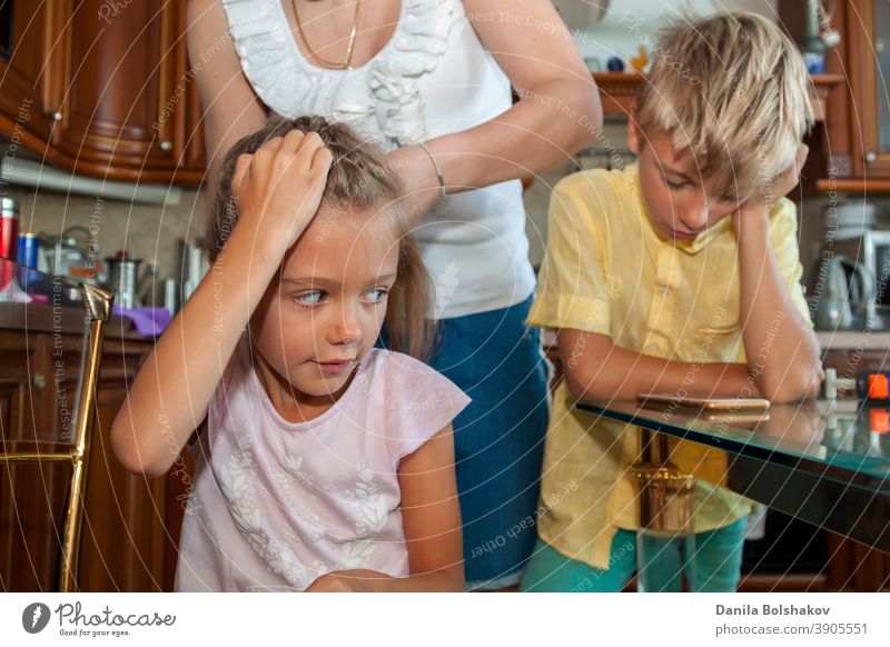 Mutter kämmt ihrer Tochter die Haare und flechtet sie, während der Junge im gelben Hemd über eine Videoverbindung mit dem Handy zu Hause kommuniziert Pflege