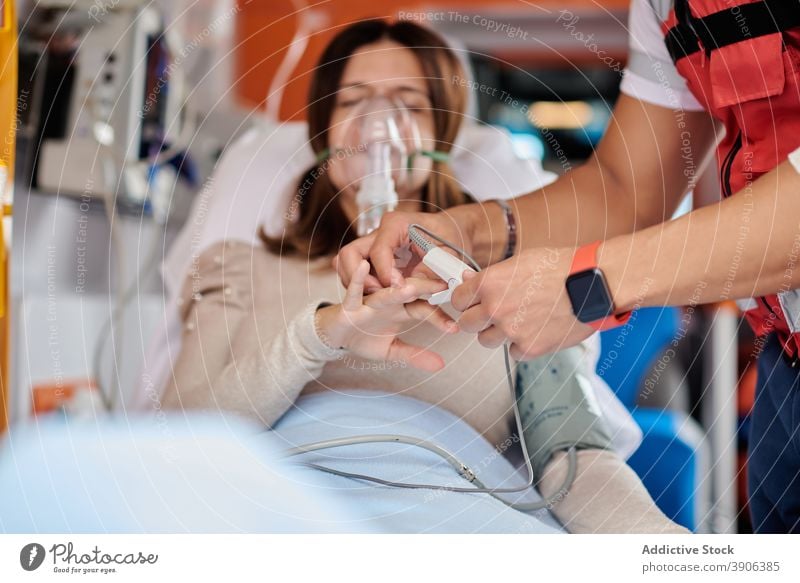 Unkenntlich gemachter Sanitäter behandelt Patient im Rettungswagen Krankenwagen PKW Notfall Puls Oximeter Beatmungsgerät Mundschutz geduldig medizinisch Trage