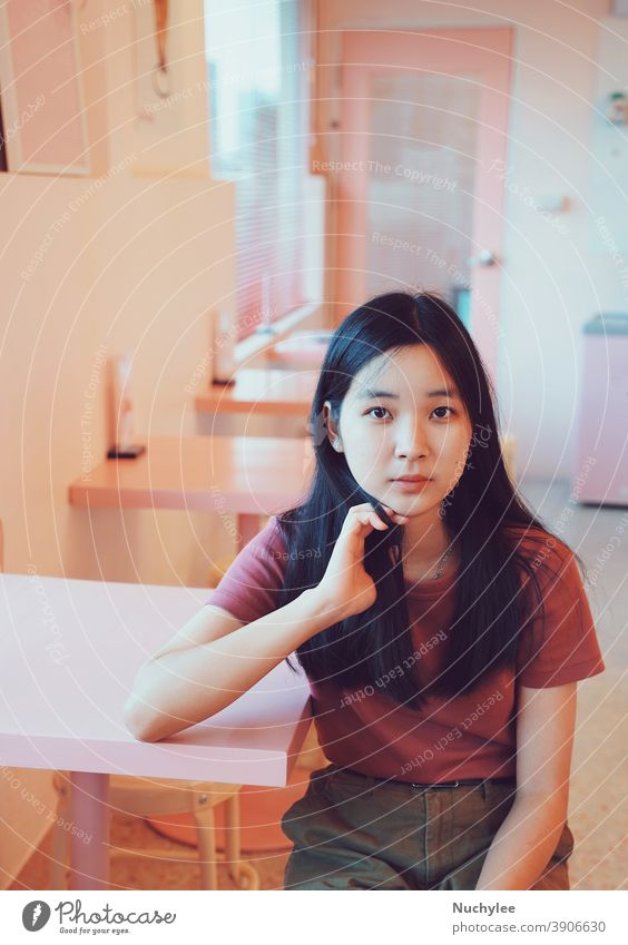 Junges asiatisches Teenager-Mädchen, süßes tausendjähriges Mädchen, das in die Kamera schaut und in einem pastellrosa Cafe sitzt, Lifestyle-Konzept Einsamkeit