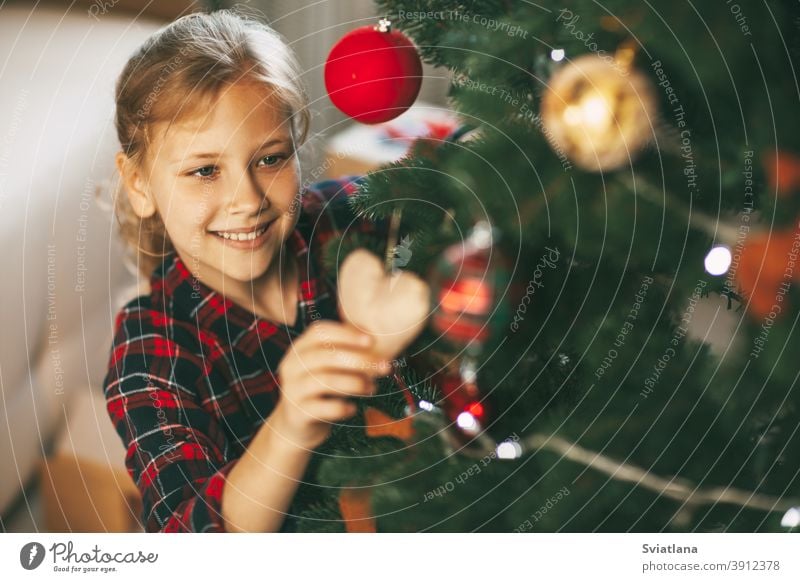 Glückliche kleine Blondine in Neujahrskleidung zu Hause, schmückt den Weihnachtsbaum und lächelt. Urlaub Konzept für Weihnachten und Neujahr zu Hause.