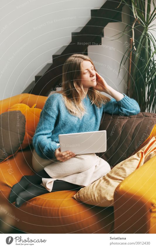 Pensive schönes Mädchen sitzt auf der Couch mit einem Laptop. Junge Frau arbeitet zu Hause mit Laptop. Arbeit online, freiberuflich, soziale Distanz Computer