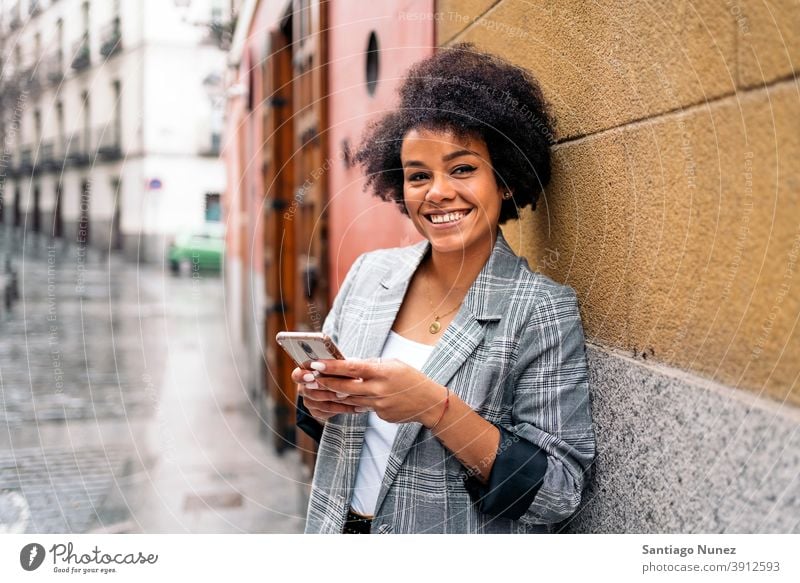 Hübsche Afro Frau mit Telefon in die Kamera schauen Afro-Look Porträt schwarze Frau per Telefon Straße Stadtleben Lächeln Funktelefon Smartphone benutzend