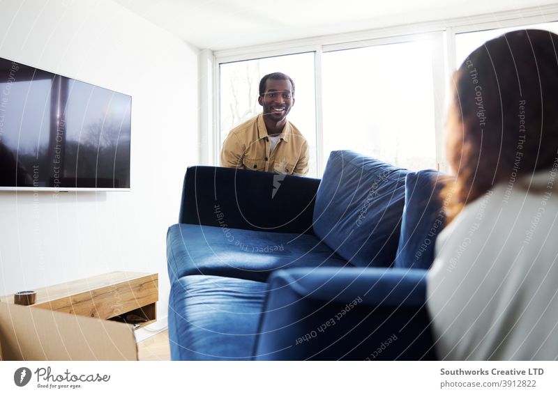 Junges Paar im neuen Zuhause trägt Sofa im Wohnzimmer am Umzugstag umgeben von Umzugskartons junges Paar Hauskauf tragen Heben Möbel räkeln Auspacken Kisten