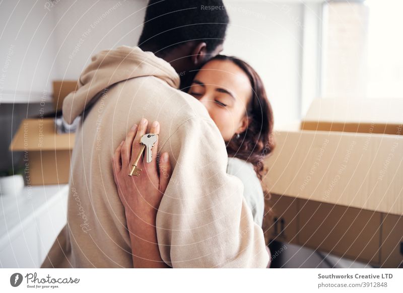Junges Paar mit Schlüssel zu neuem Zuhause umarmt, als sie Umzugskartons in der Küche zusammen auspacken junges Paar Hauskauf Auspacken Kisten Beteiligung