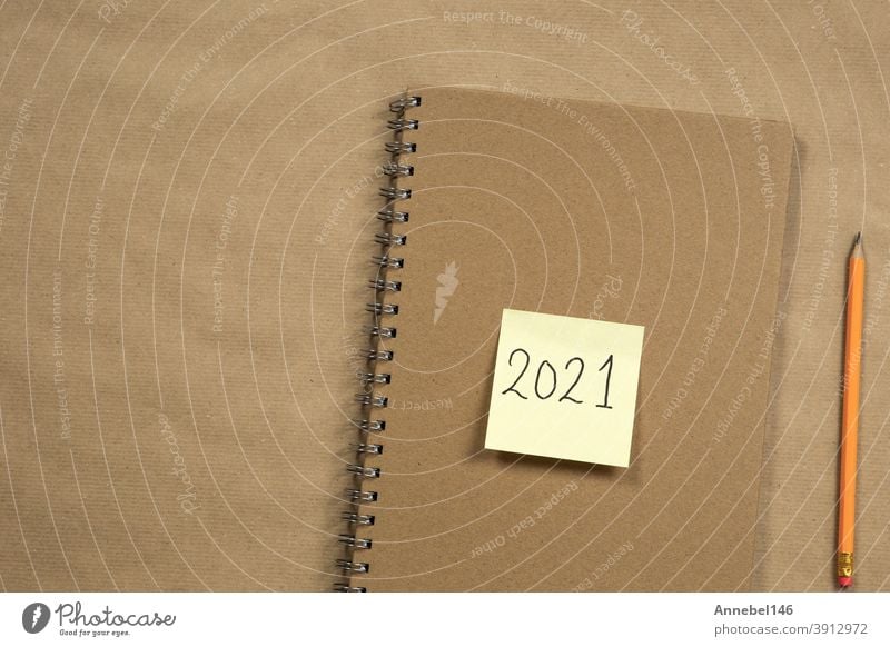 Draufsicht auf Brown Notizblock und gelbe Haftnotiz mit 2021 Neujahrsbotschaft, Bleistift auf braunem Papier Hintergrund Textur, Bildung oder Business-Konzept