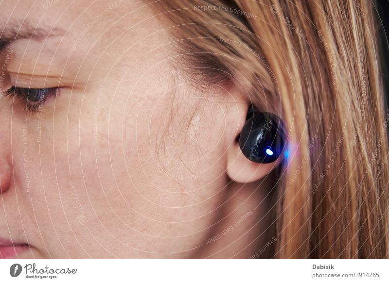 Frau hört Musik durch drahtlose Kopfhörer. Kaukasische Frau mit bluetooth Kopfhörer im Ohr, Nahaufnahme Drahtlos Audio zuhören Bluetooth schwarz Gerät digital