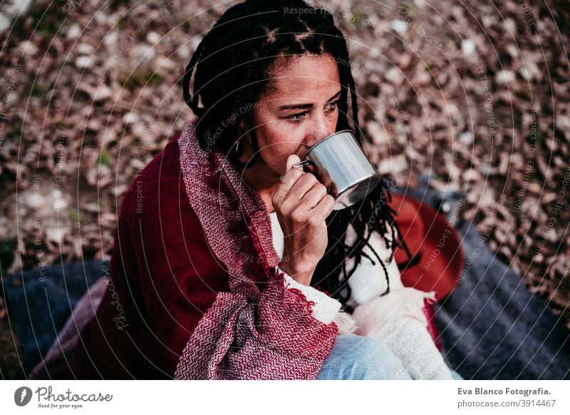 Porträt von hispanischen Mitte erwachsene Frau im Freien halten in Decke eingewickelt. Trinkwasser während picnic.Autumn Saison Herbst Afrofrau Latein