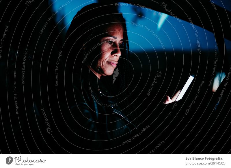 hispanische Frau mit Mobiltelefon im Auto bei Nacht. Reisen und Technologie Konzept Handy PKW Bildschirm reisen schön mittlerer Erwachsener Lebensstile klug