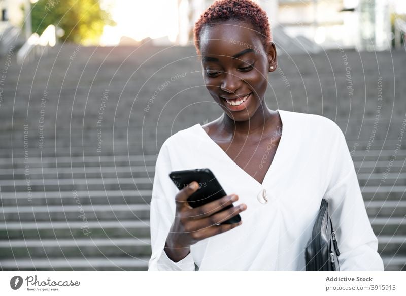Fröhliche schwarze Frau mit Smartphone auf der Straße in der Stadt Geschäftsfrau benutzend Glück lesen urban Stil Mobile Telefon Lächeln zufrieden modern jung