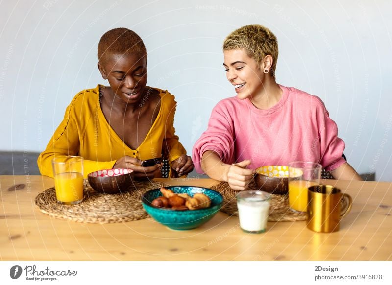 Zwei junge Frauen Paar, beste Freunde sitzen im Café, Frühstück essen und Kaffee trinken, mit Smartphone. Freundschaft häusliches Leben Zusammensein Lächeln